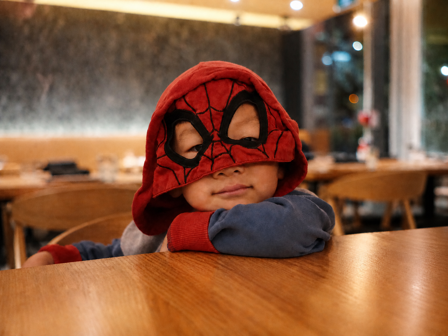 Vincent in a red masked hood, leaning on a café table